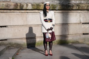PARIS, FRANCE - MARCH 08: A guest wears white pillbox hat, white sunglasses, cream double breasted blazer jacket, shiny black layered leather belts, burgundy bordeaux leather belt, black bangle bracelet, gold bangle bracelets, black sheer mesh Gucci monogram Gucci gloves, silver rings, burgundy bordeaux woven Bottega Veneta Andiamo leather bag, light blue Labubu bag charm, cream Labubu bag charm, black sheer mesh footless leggings, shiny burgundy bordeaux pointed toe heels leather shoes, outside Elie Saab, during the Paris Fashion week Women's Fall/Winter 2025-2026 on March 8, 2025 in Paris, France. (Photo by Edward Berthelot/Getty Images)