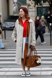 PARIS, FRANCE - MARCH 11: A guest wears red jumper, white skirt, beige long jacket, brown suede Miu Miu bag with Labubu charm, white red and blue Miu Miu sneakers, outside Miu Miu, during the Womenswear Fall/Winter 2025/2026 as part of Paris Fashion Week on March 11, 2025 in Paris, France. (Photo by Claudio Lavenia/Getty Images)