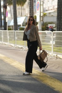 CANNES, FRANCE - MAY 15: Farina Opoku is seen wearing a cropped blazer with lapel collar in khaki green, a white ribbed v-neck t-shirt with black stripes, a small black belt with golden buckle, a black wide leg pleated pants, a pair of white canvas espadrilles with black toe cap and embroidered logo detail from Chanel, round MU52YS sunglasses with golden temples and logo detail from Miu Miu, a Kelly bag 28 Epsom Etoupe in brown leather with gold hardware from Hermès, a pink Labubu monster bag charm, a fine golden necklace with drop shaped diamond pendant from Leo Mathild, a fine golden necklace with round plate pendant, a pair of fine golden hoop earrings from Ariane Ernst Jewelry during day three of the 78th Cannes Film Festival on May 15, 2025 in Cannes, France. (Photo by by Moritz Scholz/Getty Images)