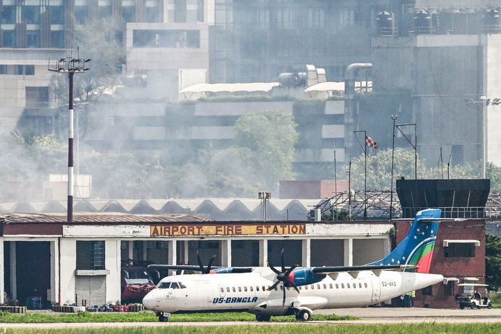 An aircraft prepares to take off as smoke rises from the fire-damaged cargo terminal of Hazrat Shahjalal International Airport.