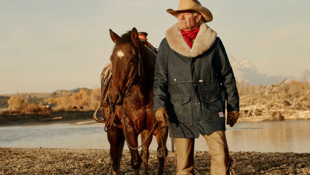 cowboy standing next to a horse while looking into the distance and wearing a filson x wrangler coat