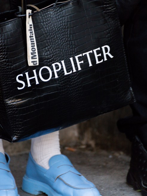 A black faux crocodile leather tote bag that reads “SHOPLIFTER” was spotted at the Louis Vuitton Menswear Spring/Summer 2026.