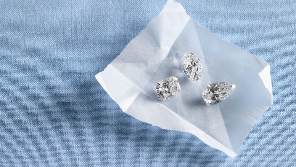 three diamonds of various shapes lying on a thin sheet of paper over a blue fabric; where to shop for loose diamonds online 2026